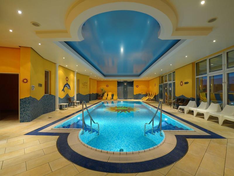 Vista interna di una piscina riscaldata in hotel con soffitto blu e sedie a sdraio bianche.