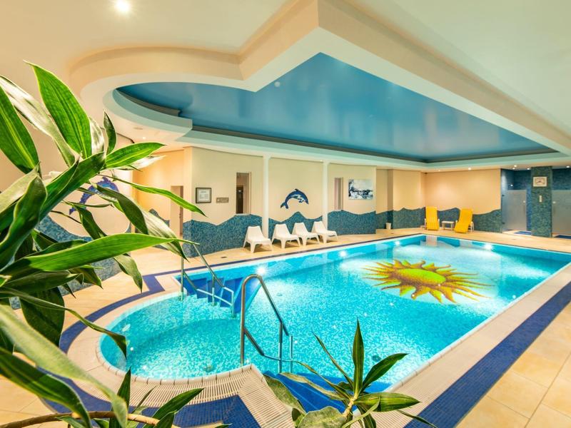 Piscina coperta ben illuminata con motivo solare, piante verdi e aree soggiorno.