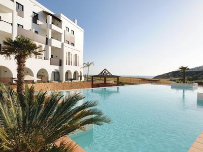 Modern hotel pool with palm trees and view of hills under clear sky.
