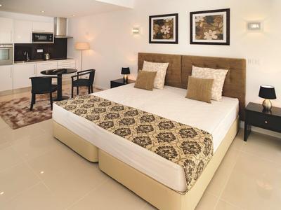 Modern hotel room with double bed, desk, kitchenette, and stylish decor.