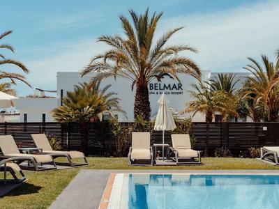 Pool with sun loungers and palm trees in front of a white building under clear sky.