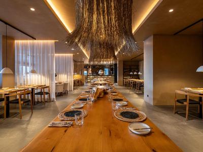 Modern restaurant with long wooden table and set places in warm lighting.