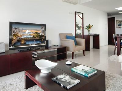 Modern furnished living room with TV, armchair, and coffee table in neutral colors.
