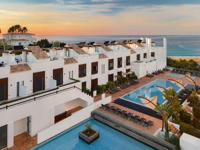 Modern white buildings with pools and sea view at sunset.