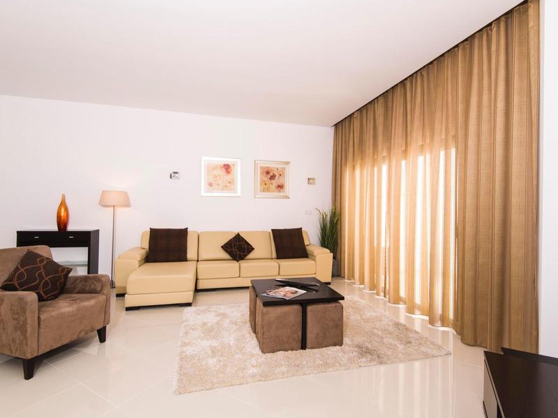 Bright hotel lounge with leather sofa, armchair, rug, and floor-length curtains.