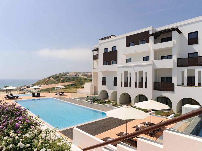Modern hotel complex with pool and sea view under clear sky.