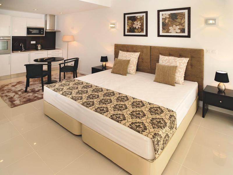Modern hotel room with double bed, desk, kitchenette, and stylish decor.