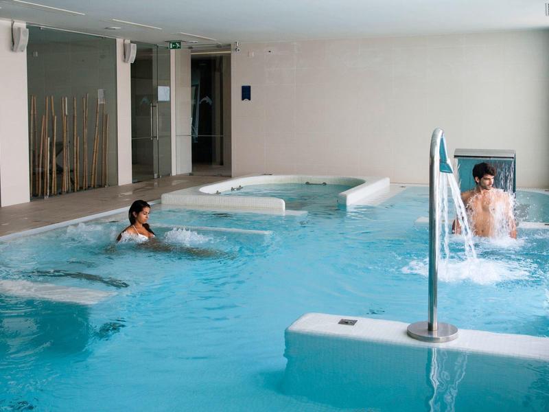 Indoor pool with two people relaxing in a hotel wellness area.
