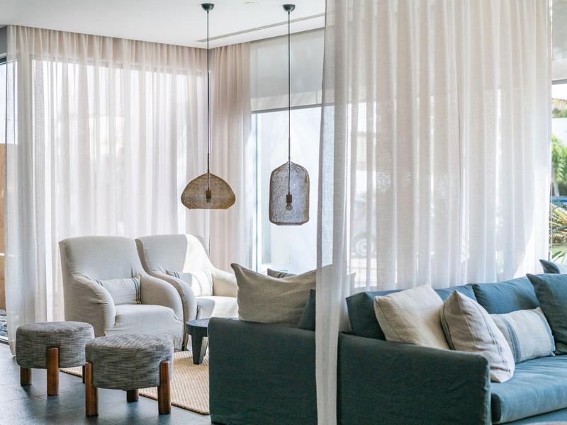 Bright hotel lounge area with armchairs, sofas, stools, and sheer curtains.
