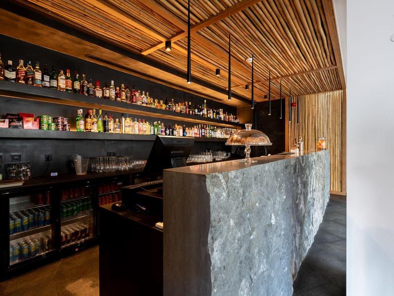 Modern hotel bar area with wooden ceiling, dark counter, and illuminated shelves full of drinks.