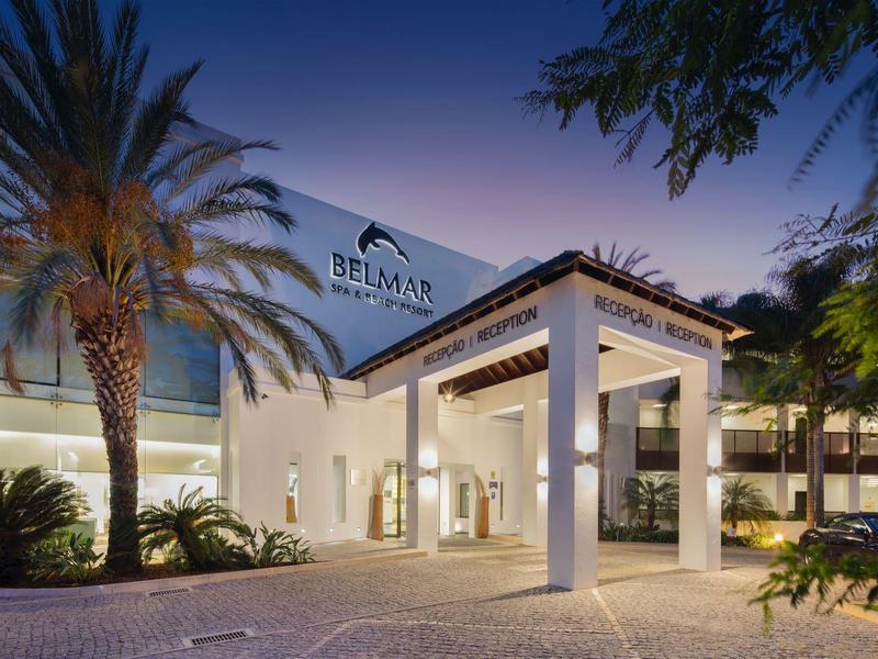 Entrance area of a modern hotel with palm trees and illuminated exterior facade at dusk.