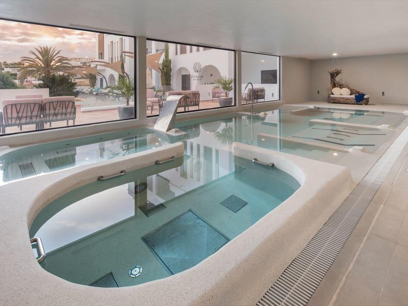 Modern indoor pool with whirlpools and large windows overlooking a terrace.