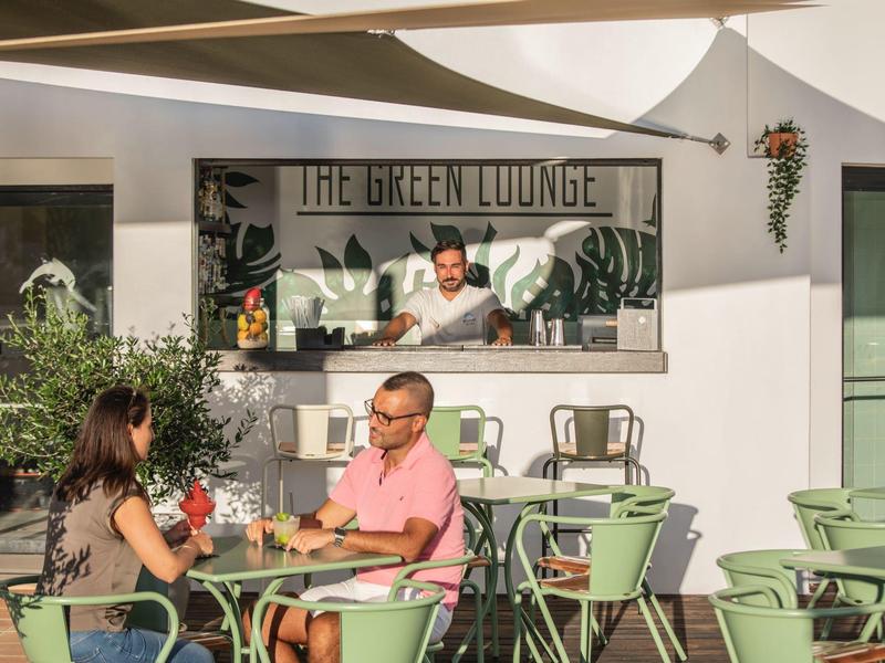 Outdoor lounge area with green chairs and a bartender behind the counter