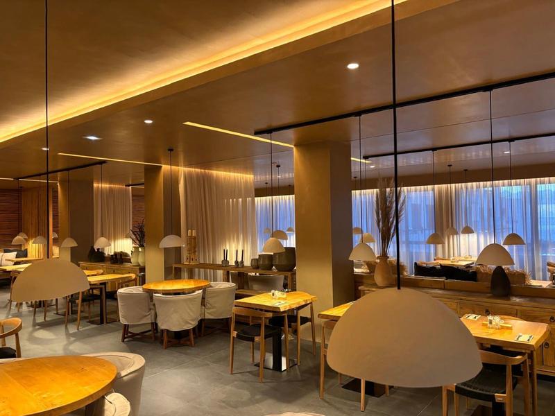 Elegant hotel dining area with warm lighting, wooden and fabric furniture, and large windows.