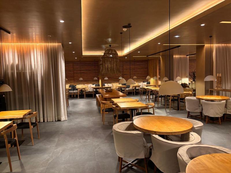 Modern dining room with wooden tables and gray upholstered chairs in warm lighting.