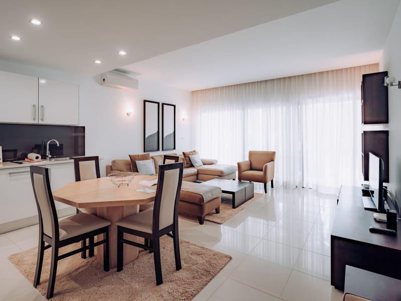 Bright living room with dining area, kitchenette, and large window with curtains.