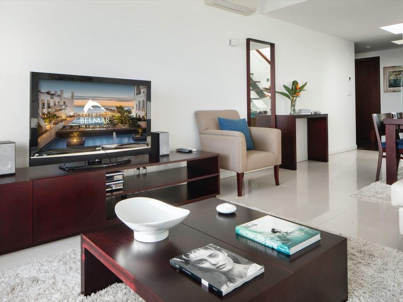 Modern furnished living room with TV, armchair, and coffee table in neutral colors.