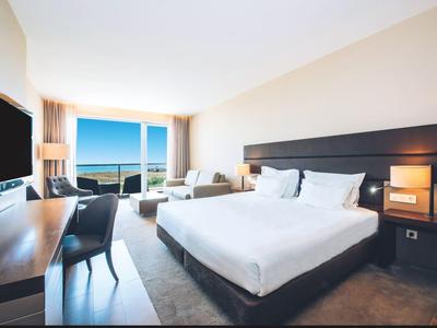 Modernes Hotelzimmer mit Doppelbett, Flachbildfernseher, Schreibtisch und Balkon mit Meerblick.