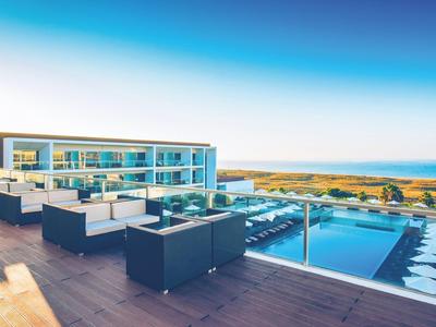 Moderne Dachterrasse mit schwarzer Lounge-Möbelgruppe, Infinity-Pool und Meerblick unter blauem Himmel.