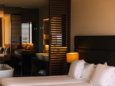 Modernes Schlafzimmer mit großem Bett, weißen Kissen, Holzlampen und Spiegeln an der Wand.