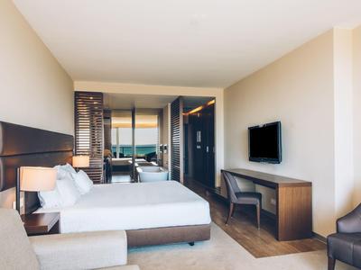 Helles Hotelzimmer mit großem Bett, Flachbildschirm, Schreibtisch und gemütlichen Sitzmöbeln.