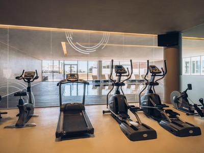 Moderne Fitnessgeräte wie Laufband und Crosstrainer in einem hellen, großen Fitnessraum mit Spiegelwand.