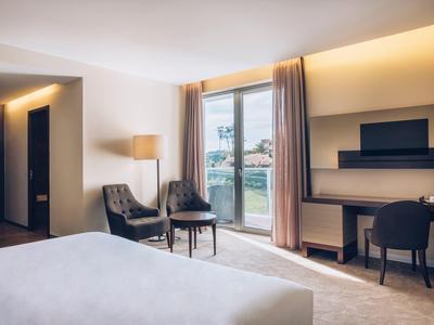 Modern eingerichtetes Hotelzimmer mit Bett, zwei Stühlen, Schreibtisch und Balkonfenster.