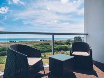 Balkon mit zwei schwarzen Stühlen und Tisch, davor grünes Land und blauer Himmel mit Wolken.