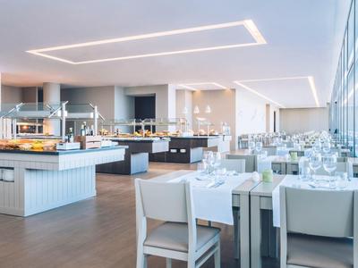 Helle moderne Restaurant mit großen Fenstern, weißen Möbeln und Buffetstationen.