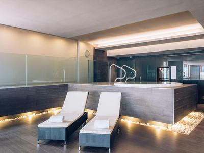 Moderner Wellnessbereich mit zwei weißen Liegen und beleuchtetem Jacuzzi in dunklem Holz.
