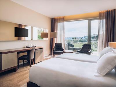 Modernes Hotelzimmer mit Doppelbett, Schreibtisch, Flachbildschirm und großem Fenster mit Bergblick.