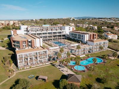 Großes Hotel mit mehreren Pools, umgeben von grünen Flächen und benachbarten Häusern.