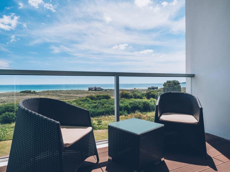 Balkon z dwoma krzesłami i stołem z widokiem na morze i zachmurzone niebo.