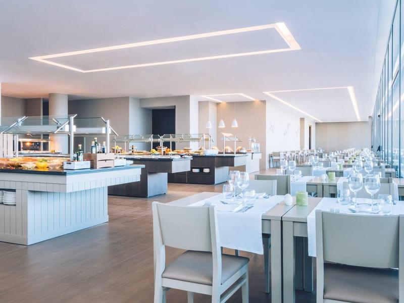 Jasna, nowoczesna restauracja z białymi krzesłami i dużymi oknami wpuszczającymi dużo światła dziennego.