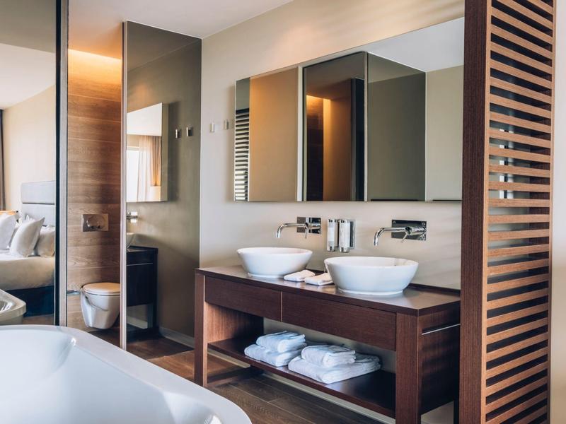 Nowoczesna łazienka z podwójnymi umywalkami, dużą wanną i stylowymi drewnianymi elementami.