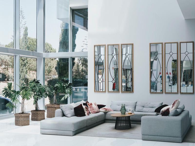 Nowoczesny salon z dużymi oknami, sofami i dekoracyjnymi lustrami.