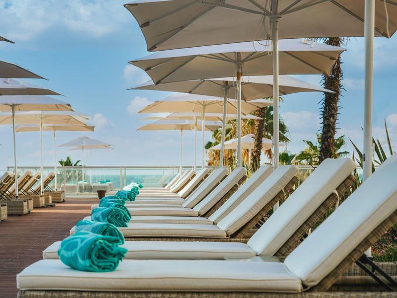 Rząd białych leżaków z turkusowymi ręcznikami pod parasolami przy basenie.