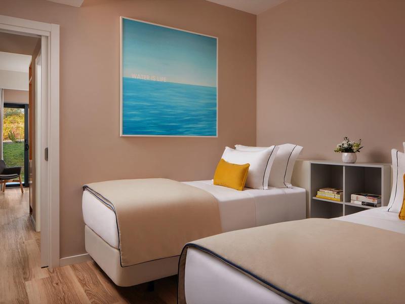 Moderne hotelkamer met twee eenpersoonsbedden, houten vloer en zee schilderij aan de muur.