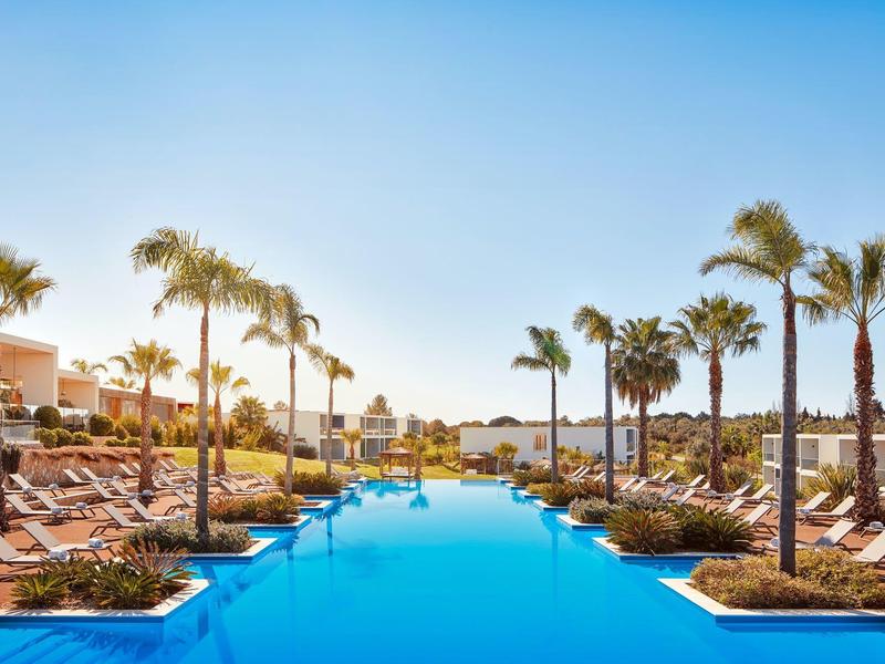 Uitnodigend hotelzwembad met ligstoelen en palmbomen onder een heldere hemel bij zonsondergang.