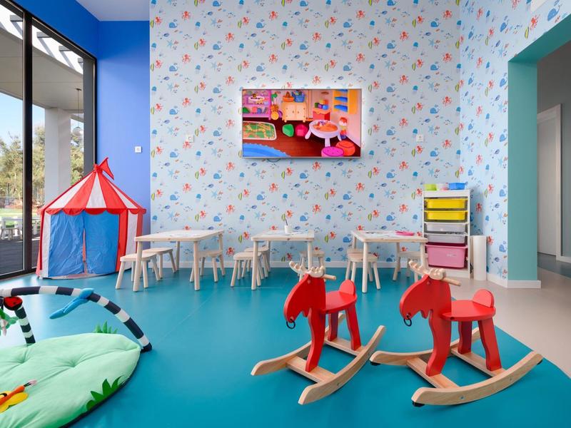 Speelruimte voor kinderen met hobbelpaardjes, tafel en stoelen, kleurrijke speeltent en wanddecoratie.