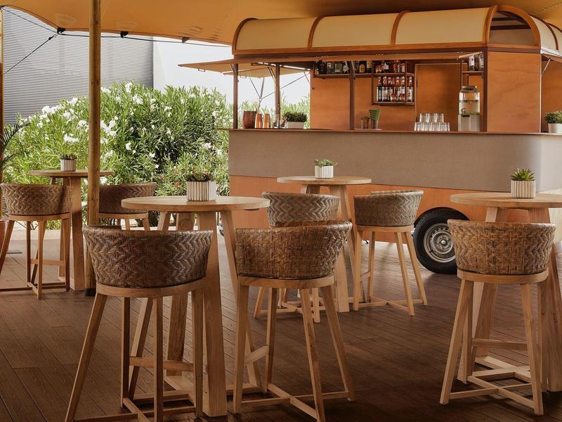 Gezellige bar met krukken en tafels onder een zonnescherm in het buitengebied van het hotel.