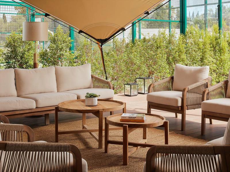 Gezellige buitenlounge met comfortabele zitplaatsen en houten tafels onder een zonnescherm.