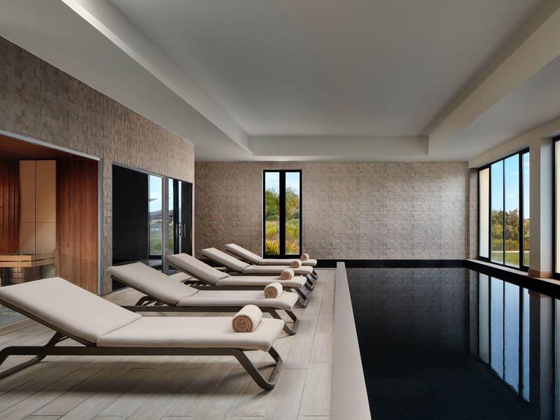 Moderne binnenzwembad met ligstoelen en grote ramen die daglicht binnenlaten.