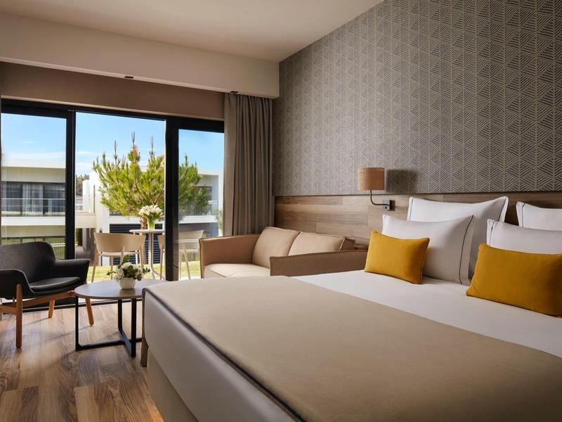 Moderne hotelkamer met tweepersoonsbed, zithoek, balkon en uitzicht op binnenplaats.