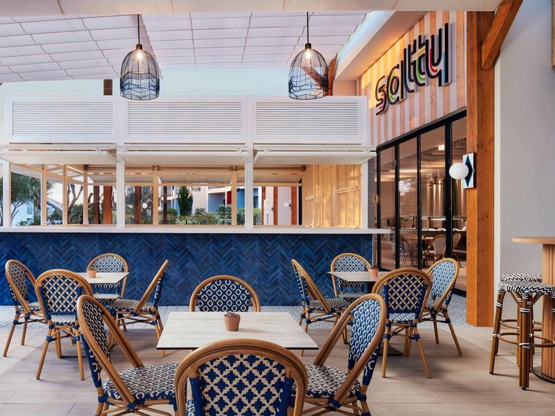 Lichte hotelruimte met blauwe stoelen, houten tafels en moderne verlichting.