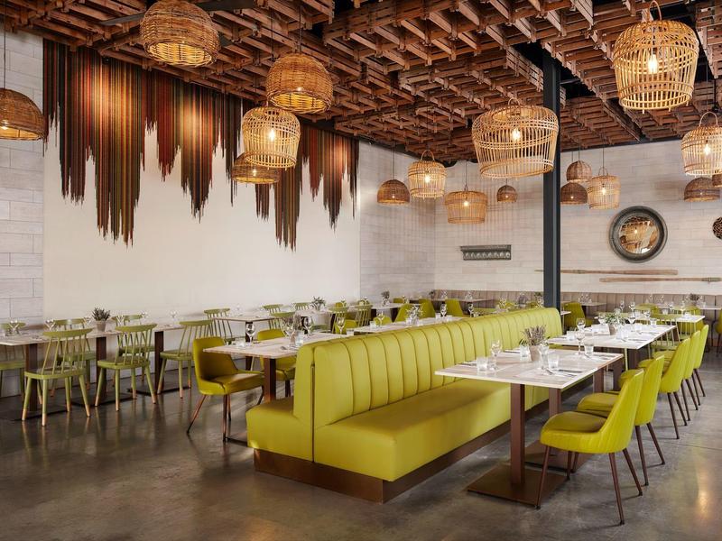 Modern restaurant met groene banken, houten tafels en hanglampen met warm licht.