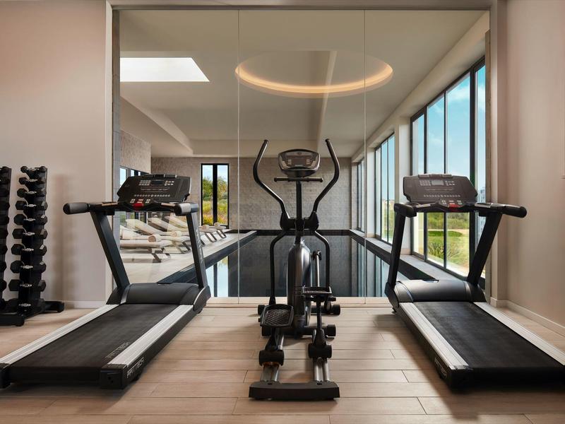 Moderne fitnessruimte met loopbanden, crosstrainer en halters bij grote ramen.