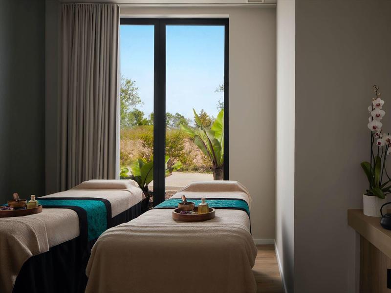 Een rustige massageruimte met drie massagetafels en tuinzicht door grote ramen.