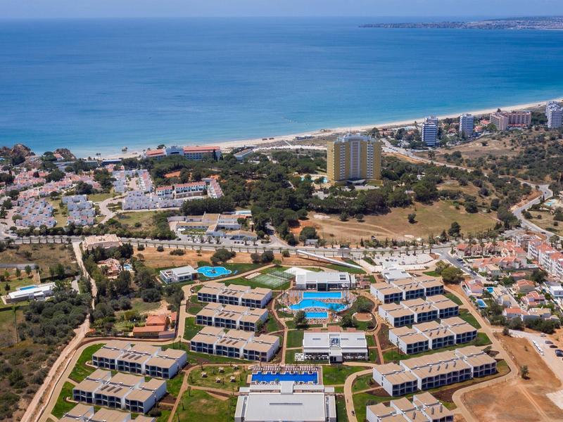 Luchtfoto van een vakantieoord aan zee met zwembaden en omliggende gebouwen.