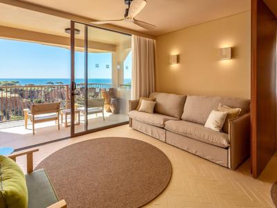 Helles Hotelzimmer mit Terrasse, Sofa, Stuhl und Blick auf das Meer.